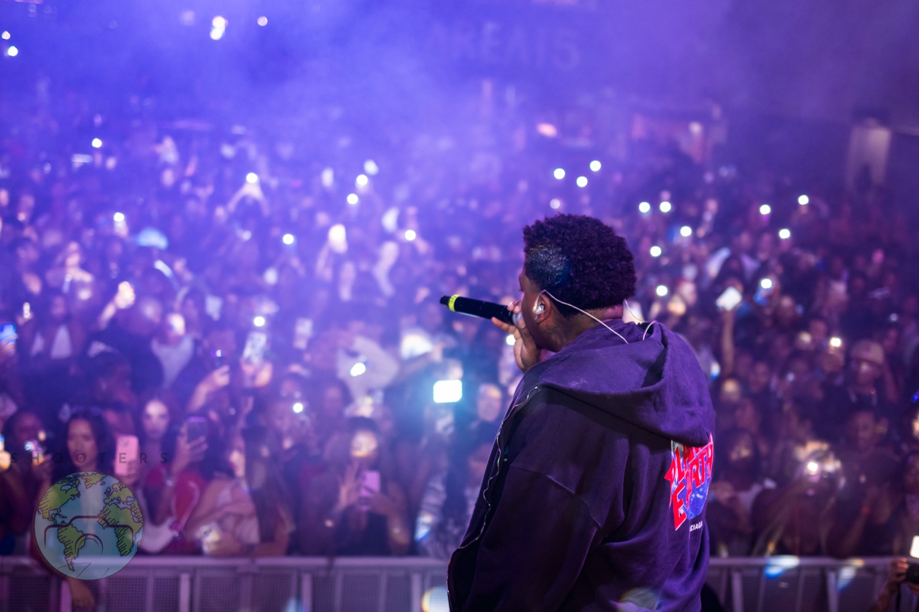 Performer facing a packed crowd under purple stage lighting at AREA15