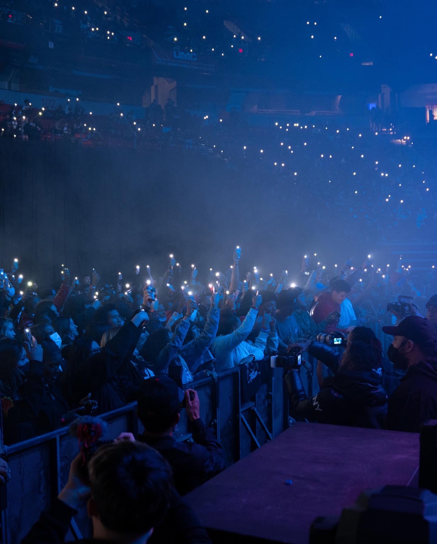 Wide arena crowd bathed in blue light and haze